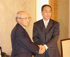 経営統合で握手する石田氏（左）と大谷氏