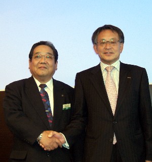 経営統合で握手する鈴木(右)、深田両社長