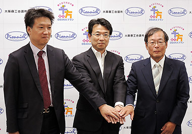 記者会見で手を取り合う相良氏（中央）、日本ベンチャーキャピタル取締役の多賀谷氏（左）、ピオニエ代表取締役の伊藤氏