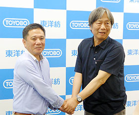 握手を交わす東洋紡の西山重雄執行役員(左)と富山大学の黒崎文也教授