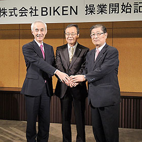 手を取り合うBIKEN財団・山西弘一理事長(右)、田辺三菱製薬・三津家正之社長(左)、BIKEN・宅康次社長