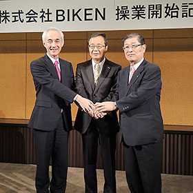 手を取り合うBIKEN財団・山西弘一理事長（右）、田辺三菱製薬・三津家正之社長（左）、BIKEN・宅康次社長