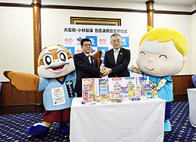 握手を交わす松井知事(左)と山根専務、大阪府のマスコットキャラクター「もずやん」と、小林製薬のキャラクタ-「熱さまくん」も登場