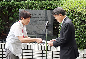 「誓いの碑」前で要望書を根本匠厚労相に渡す薬被連代表世話人の花井十伍氏(左)