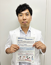 薬局で用いる減塩の説明書を持つ朝居氏