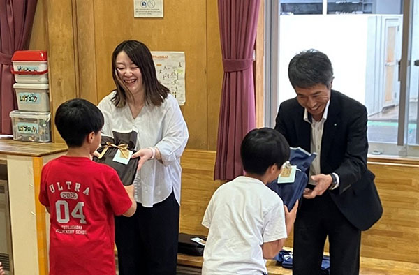 子どもたちに手渡しする井上東北支社長（右）と業務課の岩渕さん